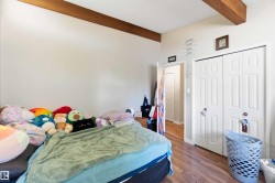 Room featuring wood-finish flooring, two exposed wood beams, and a white bi-fold closet door - 