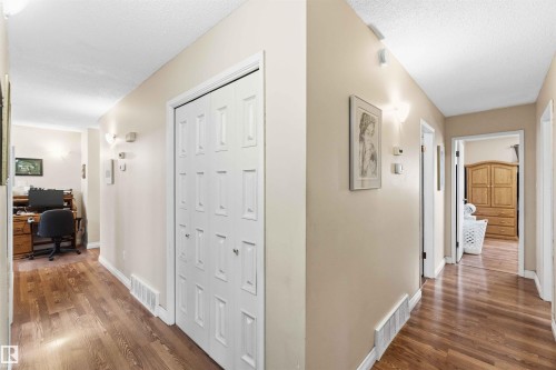 Hallway featuring wood-finish flooring, neutral wall paint, and white bi-fold doors - 13121 122 Street, Edmonton, AB 