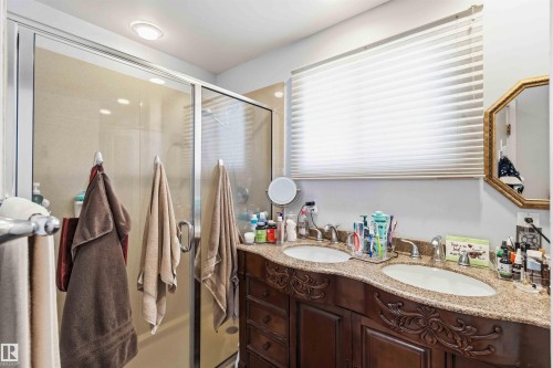 Bathroom featuring a dual sink vanity with a stone countertop, an ornate wood-finish cabinet, and a glass-enclosed shower - 13121 122 Street, Edmonton, AB 