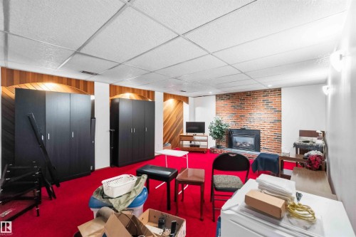 Finished space featuring a brick fireplace surround with an inset firebox, wood paneling, white walls, and a drop ceiling - 13121 122 Street, Edmonton, AB 
