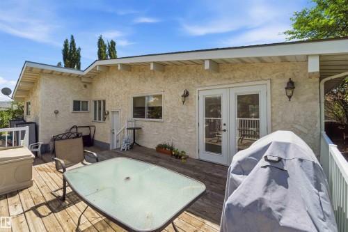 Expansive wood deck with white railing, featuring double glass-paneled doors and an exterior wall with textured stucco finish - 13121 122 Street, Edmonton, AB 
