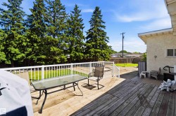 Expansive backyard featuring a large wood deck with white railings, a lower gravel patio, and a grass lawn - 