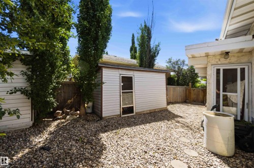 Exterior with gravel ground cover and stepping stones, featuring a detached shed with white horizontal siding and a windowed door - 13121 122 Street, Edmonton, AB 