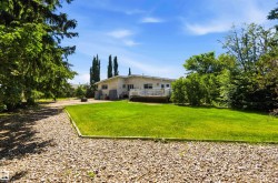 Expansive green lawn with a gravel border, featuring mature trees and a rear deck with a white railing - 