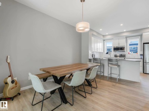 Open-concept living space featuring light wood-finish flooring, a modern dining area with a contemporary chandelier, and a kitchen island with seating - 516 35 Street, Edmonton, AB 