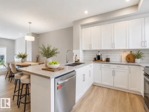 Modern kitchen featuring white shaker cabinetry, stainless steel appliances, light-toned countertops, subway tile backsplash, and wood-finish flooring - 516 35 Street, Edmonton, AB 