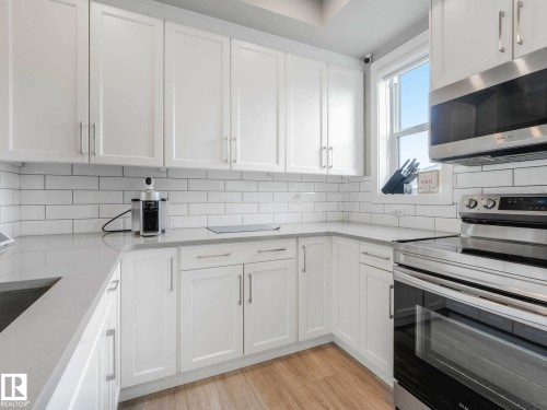 Modern kitchen featuring white shaker-style cabinetry, light-toned countertops, white subway tile backsplash, stainless steel appliances, and wood-finish flooring - 516 35 Street, Edmonton, AB 