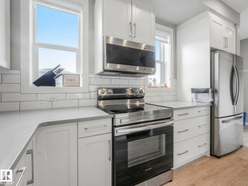 Kitchen featuring white cabinetry, stainless steel appliances, a subway tile backsplash, light-toned countertops, and wood-finish flooring - 516 35 Street, Edmonton, AB 