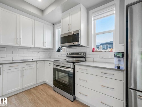 Modern kitchen featuring white shaker-style cabinetry, subway tile backsplash, stainless steel appliances, and light wood-finish flooring - 516 35 Street, Edmonton, AB 