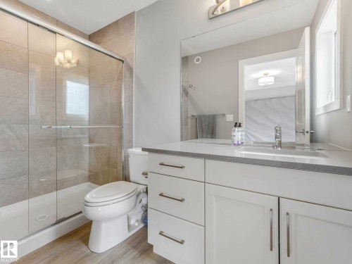Modern bathroom featuring a sliding glass shower enclosure, full wall-height tile surround, a built-in vanity with white cabinetry, and a light-toned countertop - 516 35 Street, Edmonton, AB 