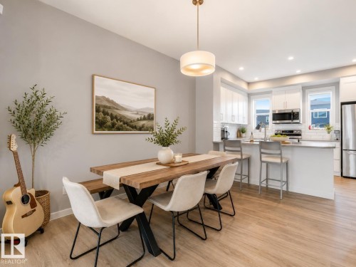 Open-concept dining area featuring wood-finish flooring, a contemporary chandelier, and light gray wall paint - 516 35 Street, Edmonton, AB 