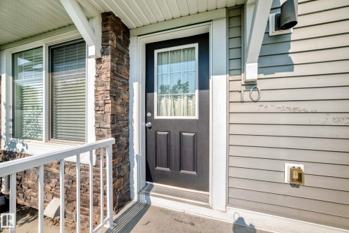 Entryway featuring a dark paneled door with an upper glass insert, complemented by a stone veneer column and light gray horizontal siding - 10-415 Clareview Rd Nw Nw, Edmonton, AB 
