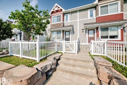 Townhome exterior featuring horizontal siding, a stone accent facade, and a white picket fence - 10-415 Clareview Rd Nw Nw, Edmonton, AB 