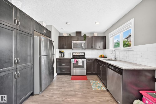 Modern kitchen featuring dark cabinetry, stainless steel appliances, light-toned countertops, a white subway tile backsplash, and wood-finish flooring - 10-415 Clareview Rd Nw Nw, Edmonton, AB 