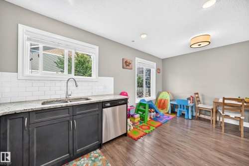 Kitchenette featuring dark-stained cabinetry, a stainless steel sink with a gooseneck faucet, light-toned granite countertops, and a subway tile backsplash - 10-415 Clareview Rd Nw Nw, Edmonton, AB 