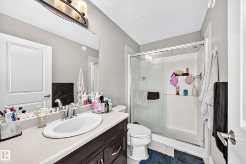 Bathroom featuring a vanity with an integrated sink, a large wall-mounted mirror, a modern three-light fixture, a toilet, and a glass-enclosed shower with a built-in shelf - 10-415 Clareview Rd Nw Nw, Edmonton, AB 