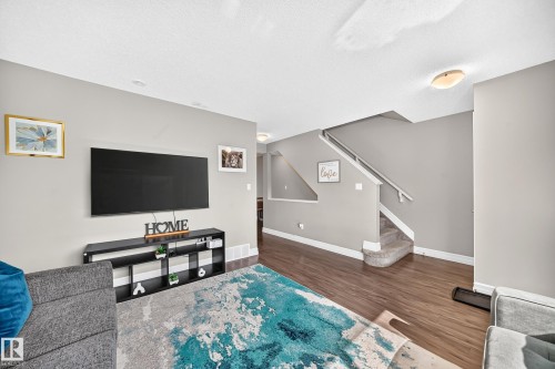 Open-concept living area featuring wood-finish flooring, a contemporary staircase with carpeted steps, and neutral painted walls - 10-415 Clareview Rd Nw Nw, Edmonton, AB 