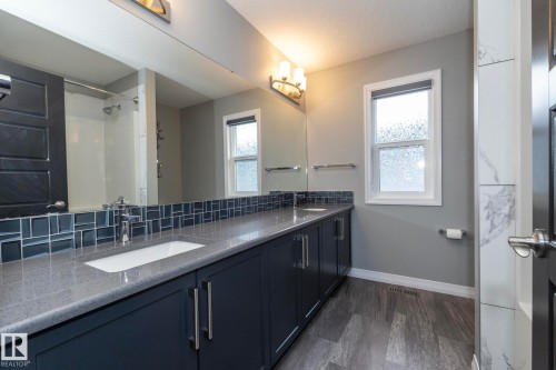 Dual vanity with undermount sinks, stone-finish countertop, and dark cabinetry - 923 Mcconachie Boulevard, Edmonton, AB 