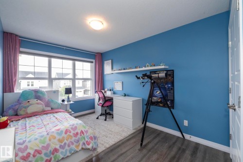 Bedroom with large window, light-colored carpeting, blue painted walls, and wood-finish flooring - 923 Mcconachie Boulevard, Edmonton, AB 