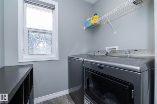 Dedicated laundry area featuring a white-framed window, overhead wire shelving, and wood-finish flooring - 923 Mcconachie Boulevard, Edmonton, AB 