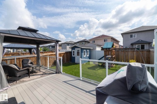Spacious backyard featuring a composite deck with glass panel railing, a built-in gazebo, and a manicured lawn - 923 Mcconachie Boulevard, Edmonton, AB 