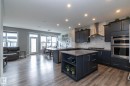 Modern kitchen featuring dark cabinetry, stainless steel appliances, a center island with counter seating, and wood-finish flooring - 923 Mcconachie Boulevard, Edmonton, AB 