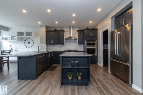 Contemporary kitchen featuring dark cabinetry, stainless steel appliances, light countertops, a central island with integrated shelving, and wood-finish flooring - 923 Mcconachie Boulevard, Edmonton, AB 