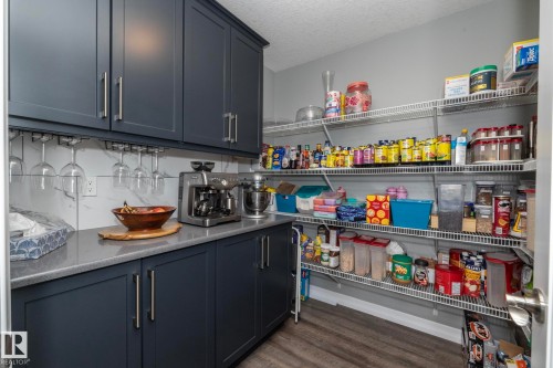 Dedicated pantry space featuring dark shaker-style cabinetry with brushed nickel hardware, grey countertops, and a white marble-patterned backsplash - 923 Mcconachie Boulevard, Edmonton, AB 