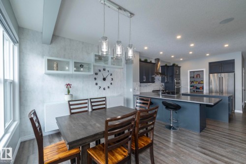 Open-concept kitchen and dining area featuring wood-finish flooring, a contemporary dining table, and a kitchen island with a stainless steel countertop - 923 Mcconachie Boulevard, Edmonton, AB 