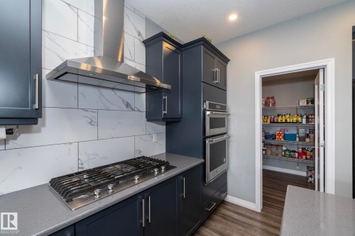 Contemporary kitchen featuring dark cabinetry, a built-in gas cooktop, and a stainless steel range hood - 923 Mcconachie Boulevard, Edmonton, AB 