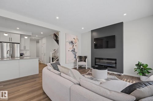 Open-concept living space featuring wood-finish flooring, recessed lighting, and a modern fireplace with a dark accent wall - 432 Roberts Crescent, Leduc, AB 