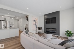 Open-concept living space featuring wood-finish flooring, recessed lighting, and a modern fireplace with a dark accent wall - 