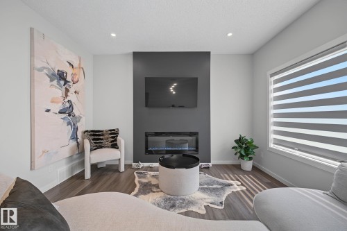 Living area featuring a dark accent wall with a built-in electric fireplace, recessed lighting, wood-finish flooring, and a large window with horizontal blinds - 432 Roberts Crescent, Leduc, AB 