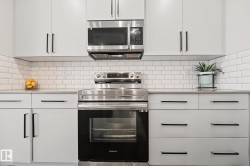Contemporary kitchen featuring white cabinetry with black bar pulls, stainless steel appliances, a white subway tile backsplash, and light-toned countertops - 