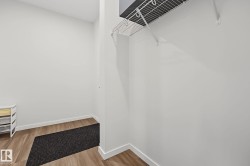 Compact storage area featuring wood-finish flooring, white walls, and a white wire shelf with a hanging rod - 