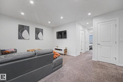 Carpeted floor area with recessed ceiling lighting, showcasing a hallway with multiple paneled doors and a visible room at the end - 432 Roberts Crescent, Leduc, AB 