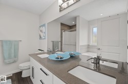 Bathroom featuring a dual vanity with undermount sinks and chrome fixtures, a large wall-mounted mirror, wood-finish flooring, and a window above the soaking tub - 