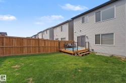 Expansive fenced backyard featuring a wooden deck with glass panel railings and a two-step entry - 