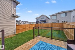 Expansive backyard featuring a natural wood deck with glass panel railings, a manicured lawn, and a perimeter wood fence - 