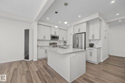 Modern kitchen featuring light gray cabinetry, stainless steel appliances, a center island with a sink, white subway tile backsplash, and wood-finish flooring - 