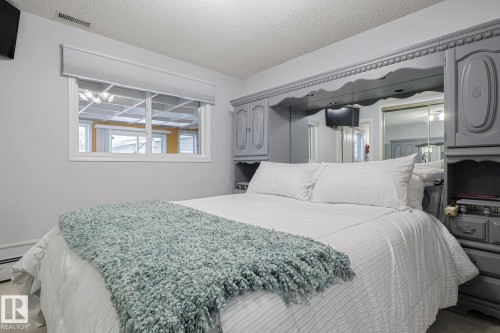 Bedroom featuring a multi-pane window with a roller shade, light gray walls, built-in mirrored cabinetry, and textured ceiling - 13304 70 Street, Edmonton, AB 