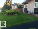 Landscaped front yard featuring a verdant lawn, a stone-edged garden bed with mature shrubs, and a decorative retaining wall - 13304 70 Street, Edmonton, AB 