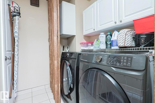 Dedicated laundry area featuring tile flooring, white shaker-style cabinetry, and a built-in wire shelf - 13304 70 Street, Edmonton, AB 