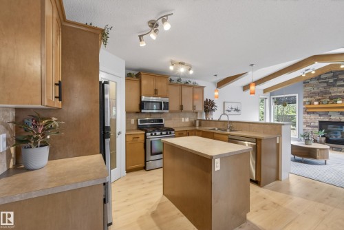 Kitchen featuring wood-finish cabinetry, stainless steel appliances, a center island, and wood-finish flooring - 2696 Anderson Crescent, Edmonton, AB - Indoor Photo Showing Kitchen With Double Sink