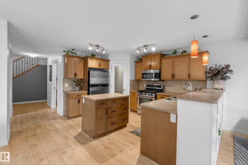 Kitchen featuring wood-finish flooring, stainless steel appliances, a central island, light wood cabinetry, and pendant lighting - 2696 Anderson Crescent, Edmonton, AB - Indoor Photo Showing Kitchen