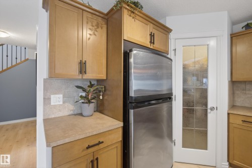 Kitchen area featuring light wood cabinetry with dark hardware, a stainless steel refrigerator, and a textured backsplash - 2696 Anderson Crescent, Edmonton, AB - Indoor Photo Showing Kitchen
