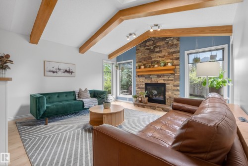 Vaulted ceiling with exposed wood beams, stone fireplace with wood mantel, large windows, and light wood-finish flooring - 2696 Anderson Crescent, Edmonton, AB - Indoor Photo Showing Living Room With Fireplace