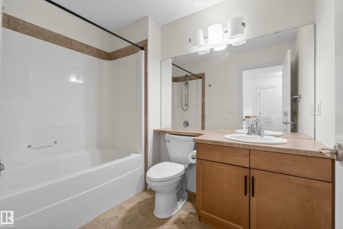 Bathroom featuring a white bathtub and shower surround with accent tile, a wood-finish vanity with a light-colored countertop, and a large mirror - 2696 Anderson Crescent, Edmonton, AB - Indoor Photo Showing Bathroom