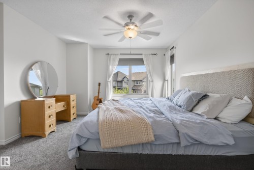 Bright bedroom featuring a large window, plush gray carpeting, white walls, and a ceiling fan with integrated lighting - 2696 Anderson Crescent, Edmonton, AB - Indoor Photo Showing Bedroom