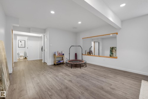 Spacious lower level featuring light gray wood-finish flooring, recessed lighting, and a large wall-mounted mirror with a wood frame - 2696 Anderson Crescent, Edmonton, AB - Indoor Photo Showing Other Room